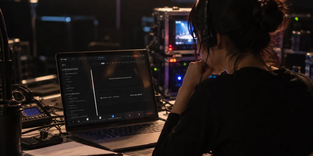 Theatre subtitle operator monitoring prepared cues at a laptop in a dark control booth