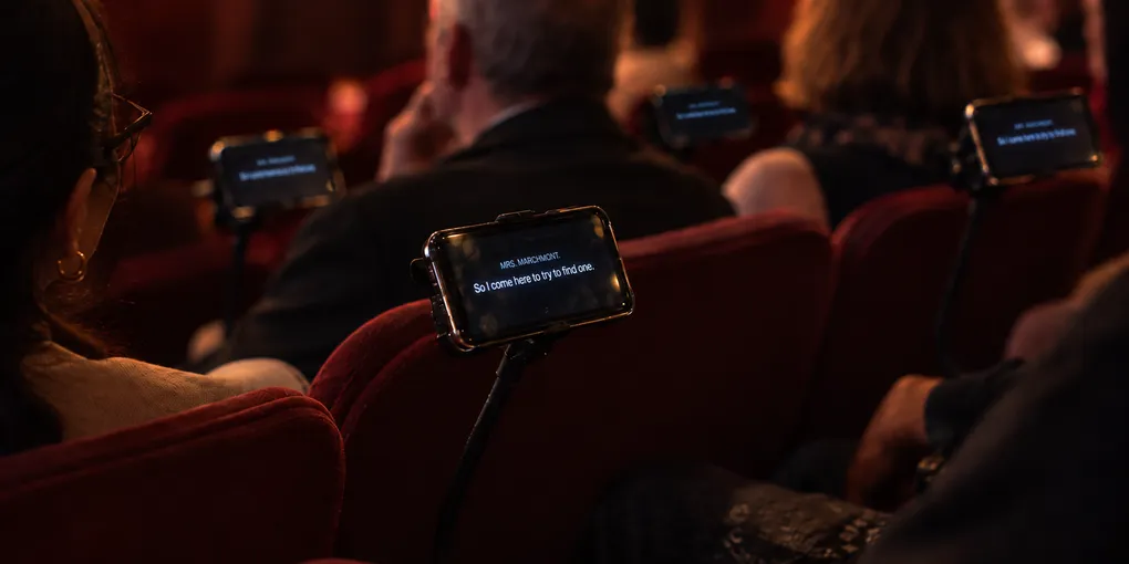 Audience members reading mobile surtitles on managed phones during a theatre performance